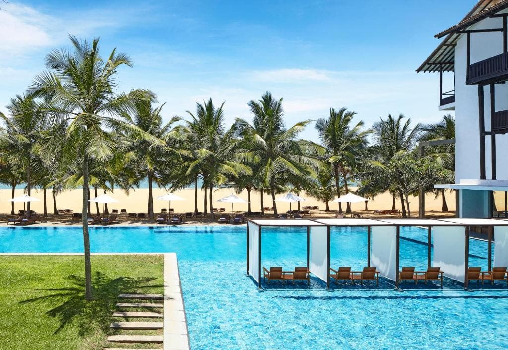 A palm-lined resort pool with cabanas toward the beach